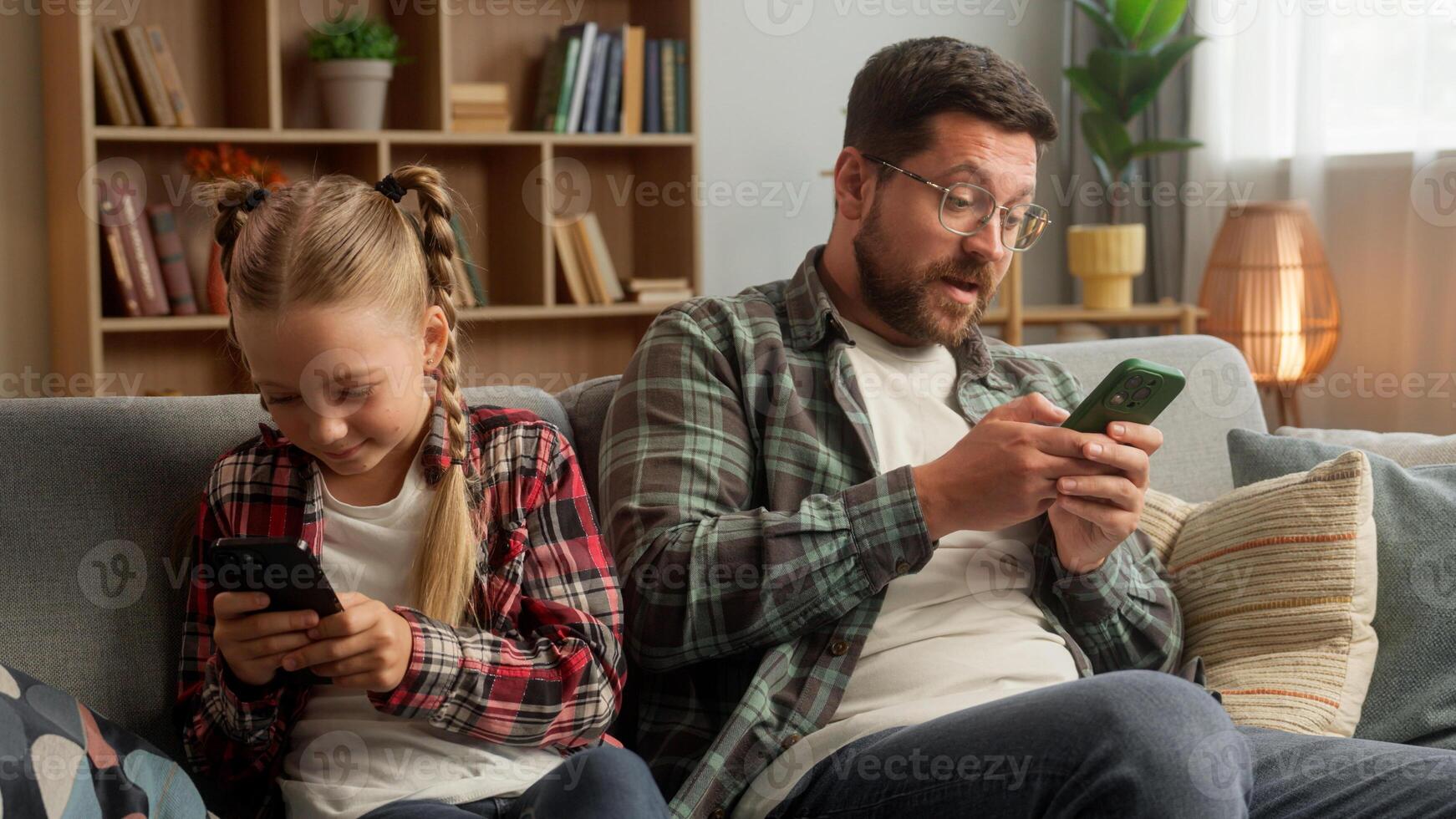 Caucasian Internet addicted male dad guy man kid daughter family using mobile phone smartphone dependency at home sofa little girl child parent father playing digital game online family technology app photo