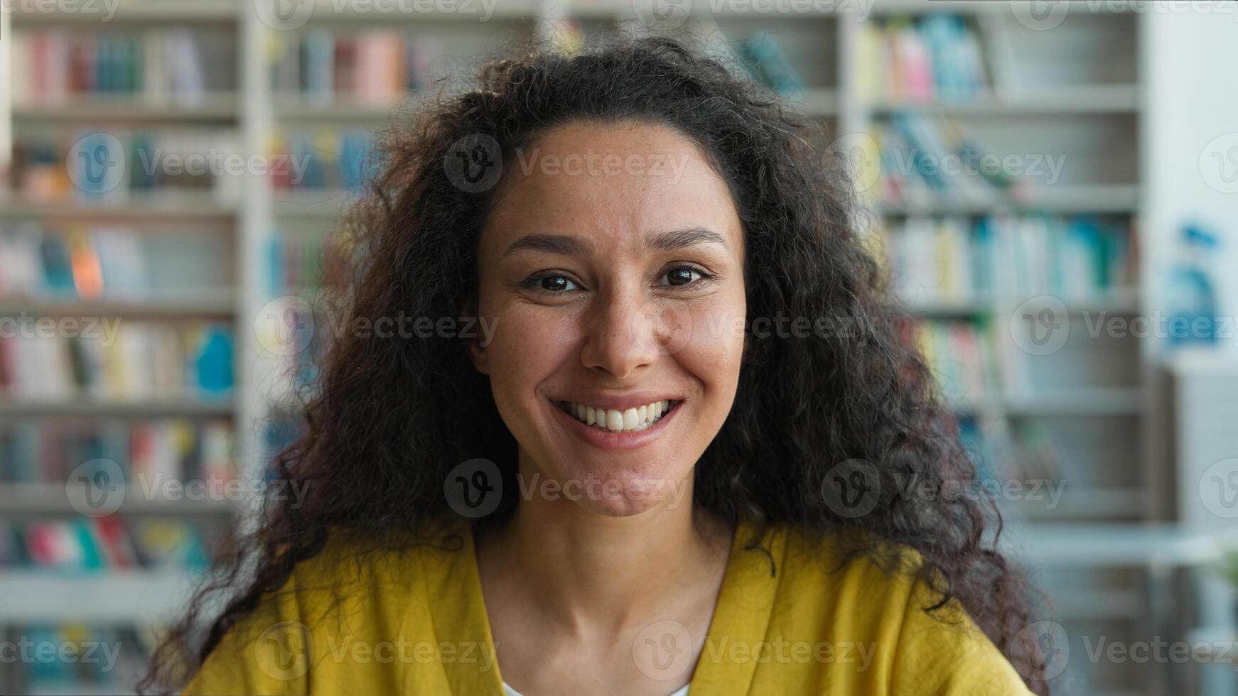 Happy Indian Caucasian woman university library bookshelf smile laughing girl student lady looking at camera female portrait high school college educated learn bookstore study face expression teenager photo
