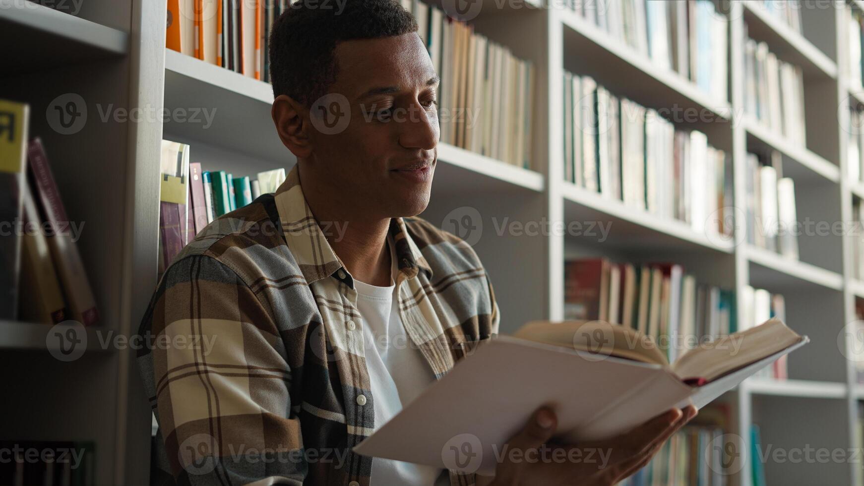 African American man sitting library floor bookcase reading book pleasure hobbies story knowledge learning student turning pages male guy academy study literary university history interesting reader photo