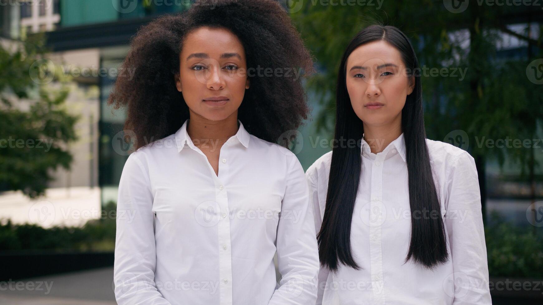Successful confident African American Asian Korean Chinese women females colleagues coworkers businesswomen business standing posing looking at camera professionals city outside office team two people photo