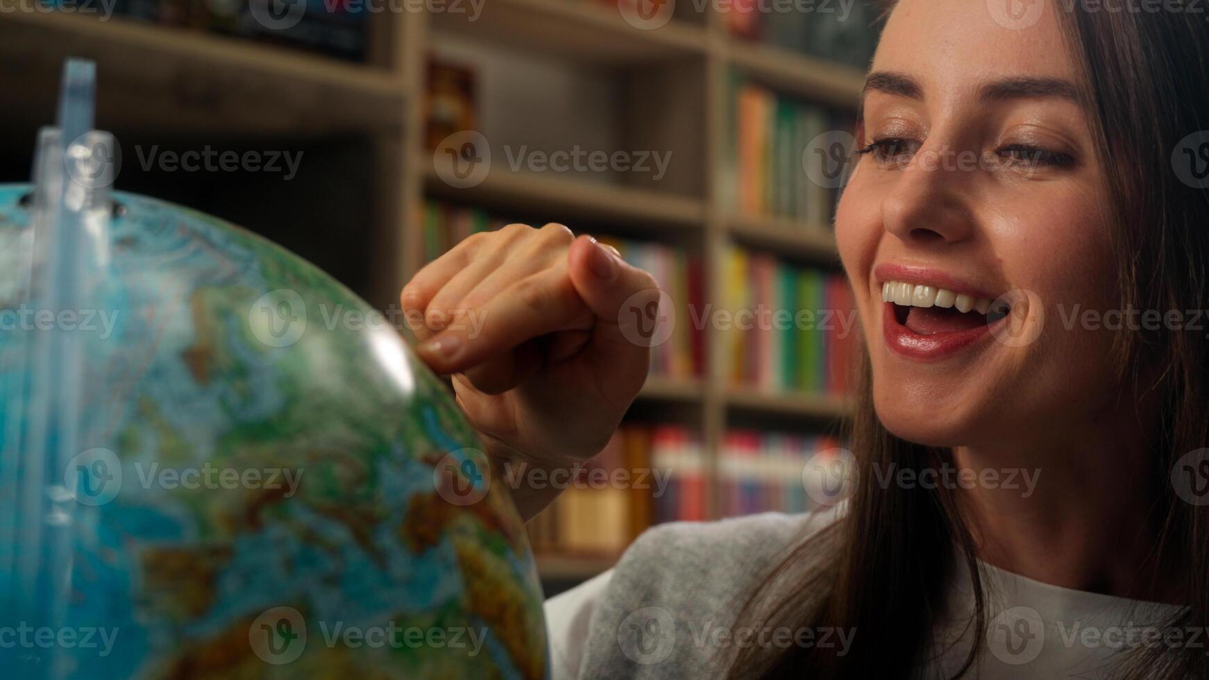 Excited Caucasian woman female girl student teacher library school geography lesson model planet earth spinning dreaming choose country vacation globe pointing finger campus learner college university photo