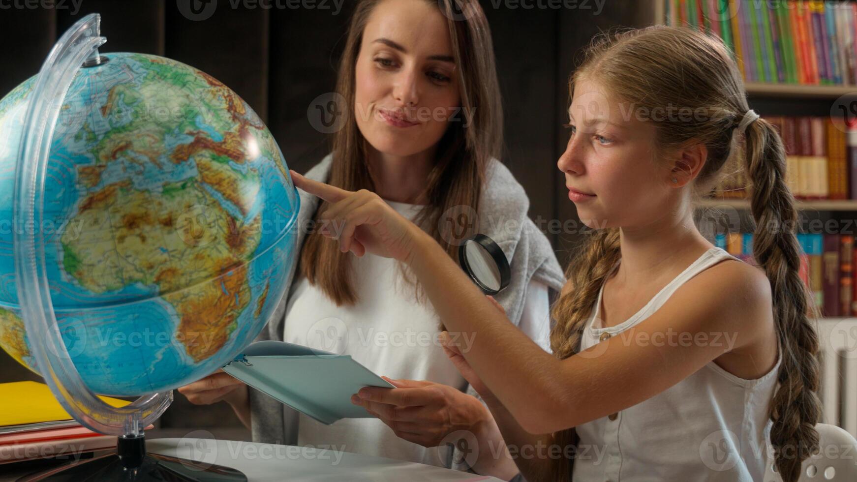 Caucasian woman female little girl teacher schoolgirl pupil school child kid learning exploring search globe world map study geography tutor desk class watch magnifying glass education student planet photo