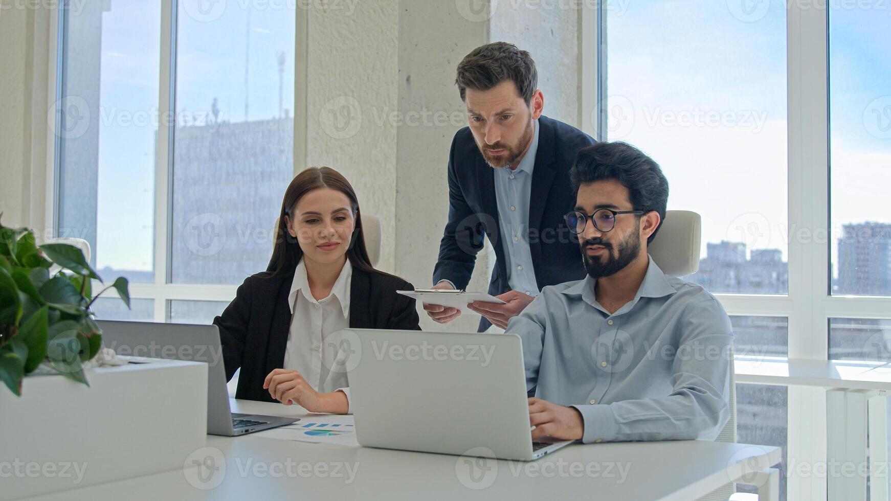 Male CEO boss leader man businessman help office coworkers with computer work check online project on laptop talking to diverse multiracial business team colleagues brainstorm analyze sales paperwork photo