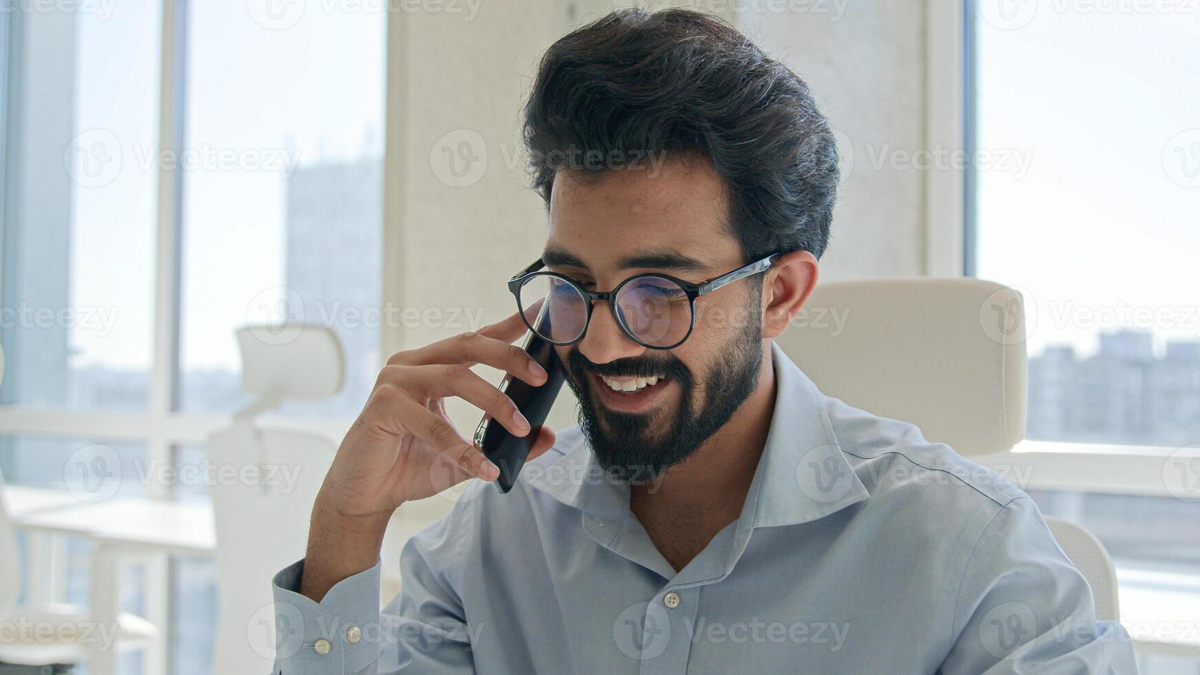 Smiling Arabian businessman manager employer Indian man busy talking cellphone working laptop in office male entrepreneur call mobile phone business discussion consulting corporate client remote chat photo