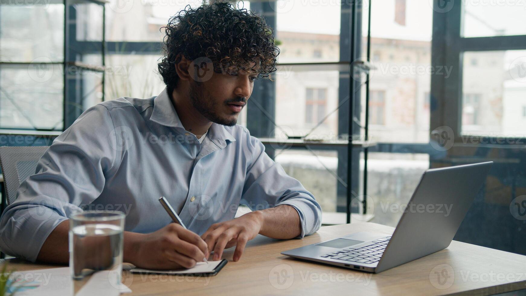 Indian Arabian man accountant writer business entrepreneur businessman write notes in notebook latino guy writing ideas report paperwork on office table studying online with laptop educational course photo