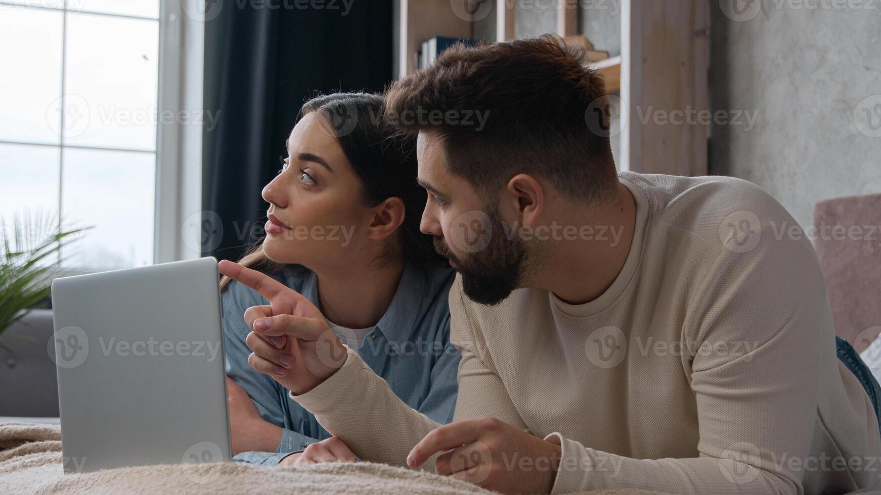 Relaxed couple family lying on bed use computer laptop online shopping together make order internet purchase choosing home goods for bedroom interior Caucasian woman man clients search delivery store photo
