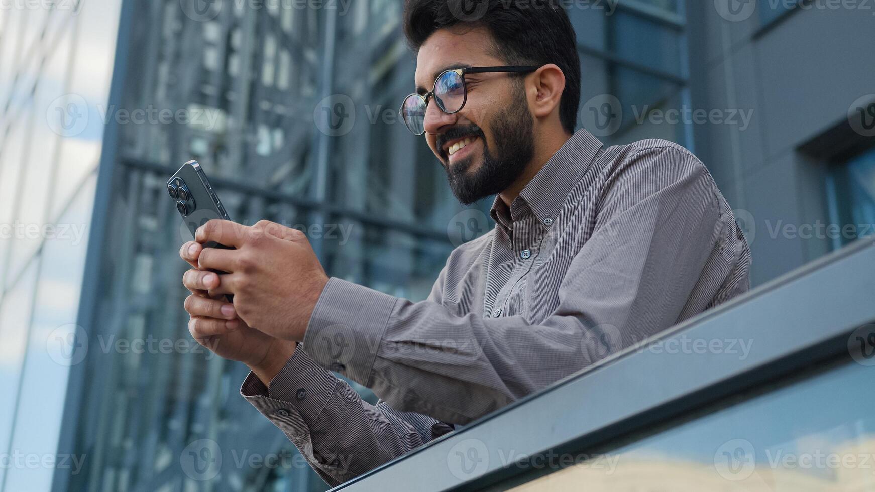 Indian Arabian man male entrepreneur worker smart businessman office manager hold mobile phone outdoors online chatting create business idea insight gesture texting message browsing smartphone in city photo