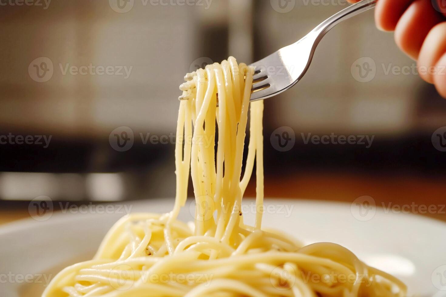 Close-up of a hand holding a fork with spaghetti over a plate in the kitchen photo