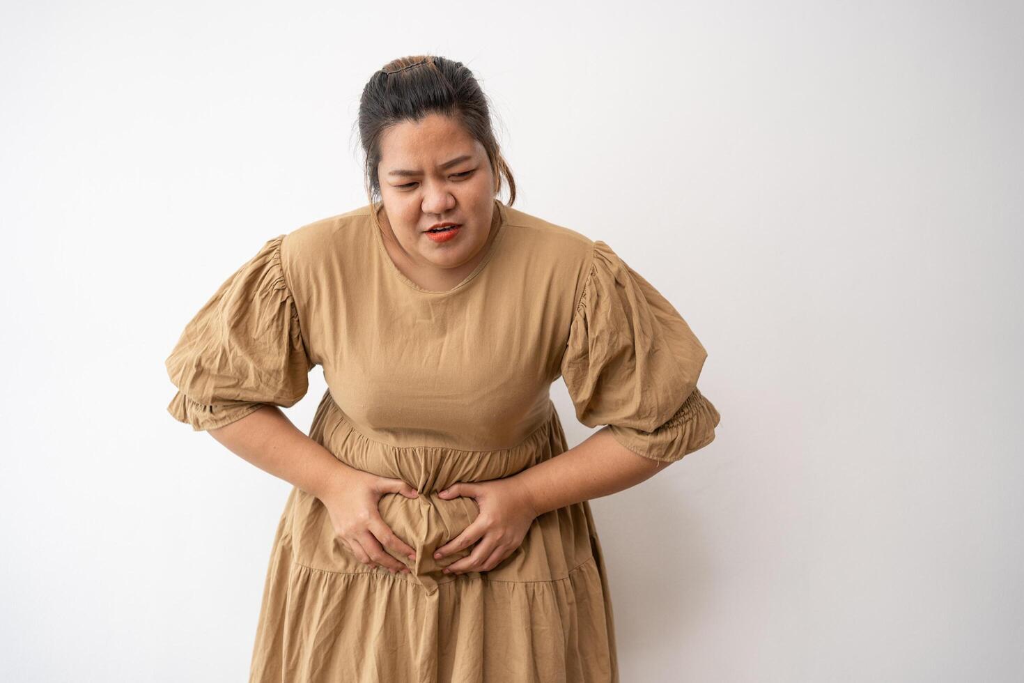 Young Asian plus size woman hand on stomach because nausea, painful disease feeling unwell, may develop gallstones or Cholecystitis. From gastritis and enteritis to people and health care concepts. photo