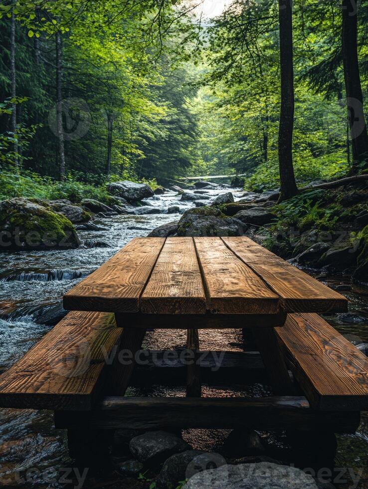 A wooden picnic table by a serene stream surrounded by lush greenery. photo