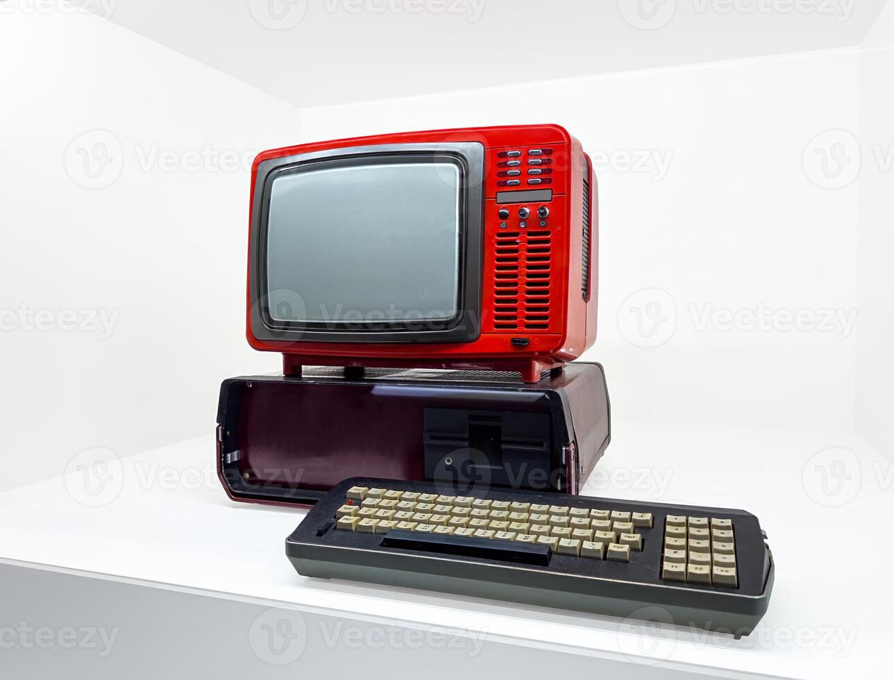 This image displays a retro computer terminal featuring a vibrant red monitor with ventilation panels and control buttons. The setup includes a vintage keyboard with beige and black keys, showcasing photo