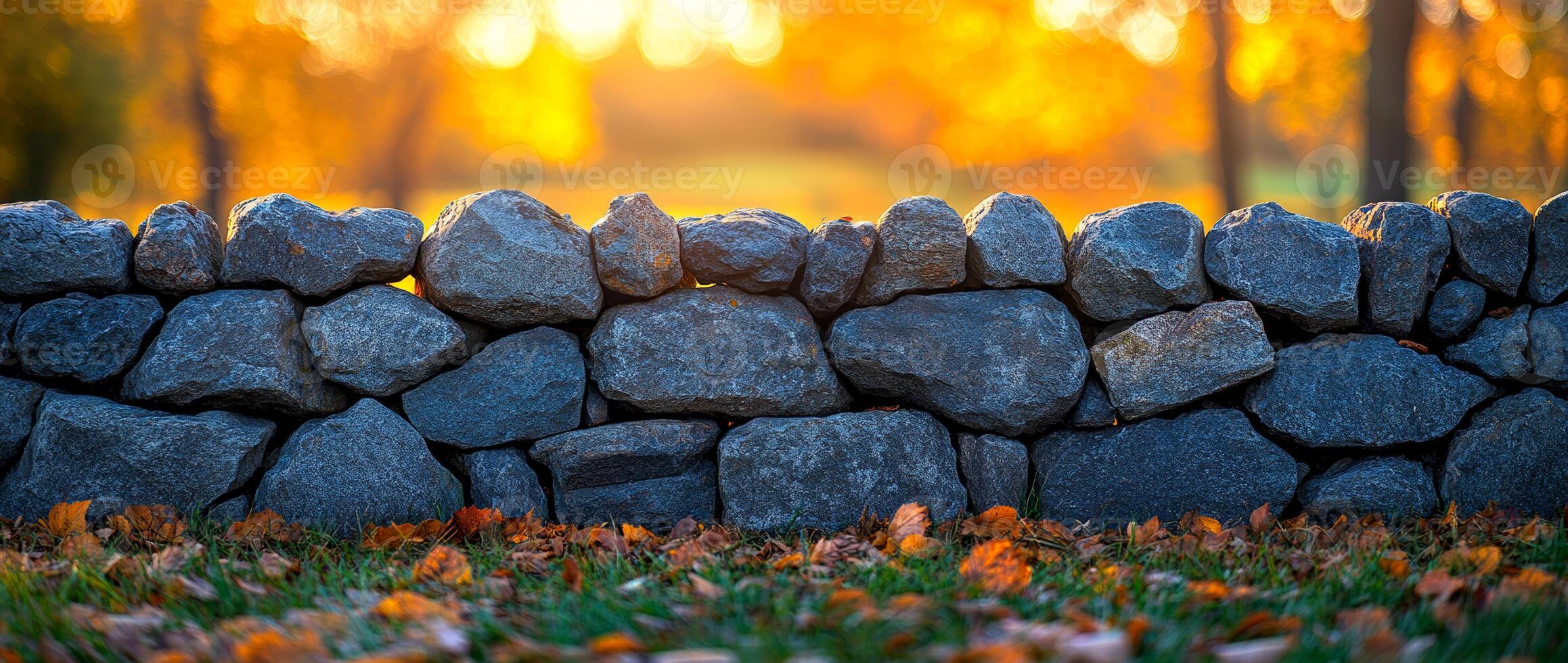 A wall made of rocks with leaves on the ground in front of it. The wall is tall and the leaves are scattered around it photo