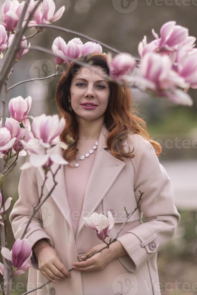 Woman magnolia flowers, surrounded by blossoming trees., hair down, wearing a light coat. Captured during spring, showcasing natural beauty and seasonal change. photo
