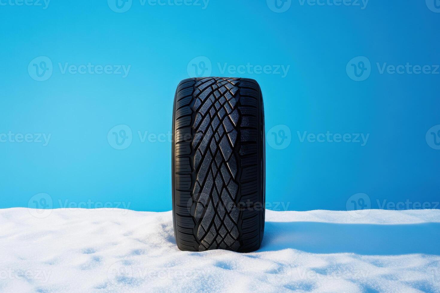 Winter tire placed on snow against a bright blue background showcasing tread design and winter conditions photo
