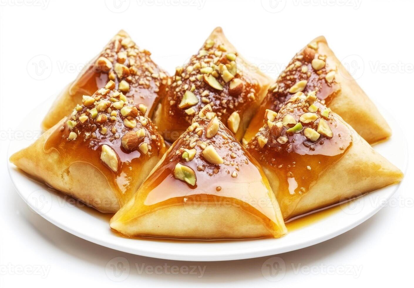Sweets served on a white plate showcasing mouthwatering triangular pastries topped with nuts and syrup photo