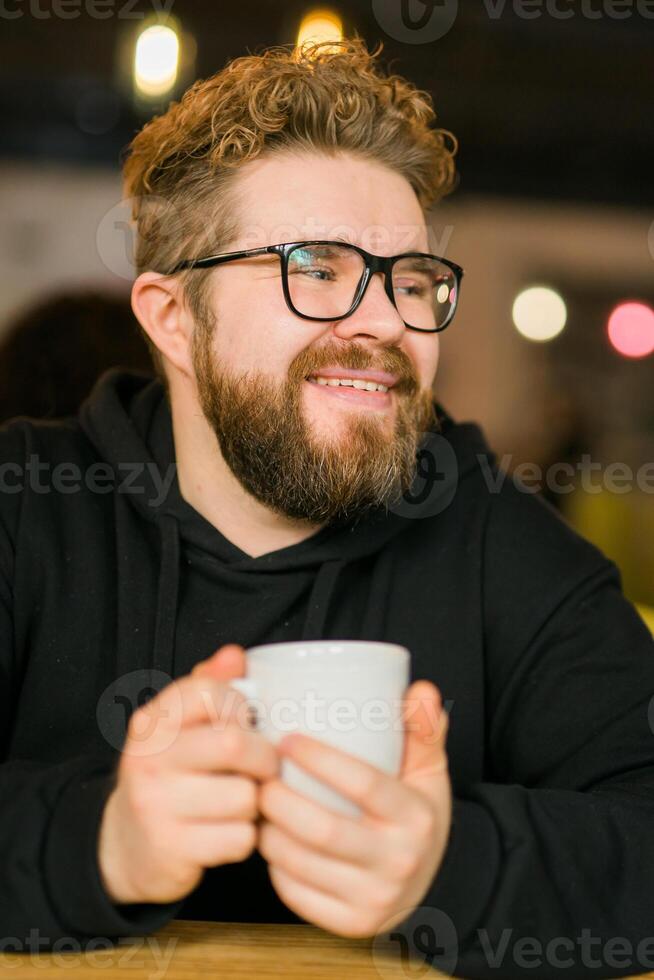 Bearded curly man smiling confident drinking coffee in restaurant or coffee shop. Millennial generation and Gen Y photo