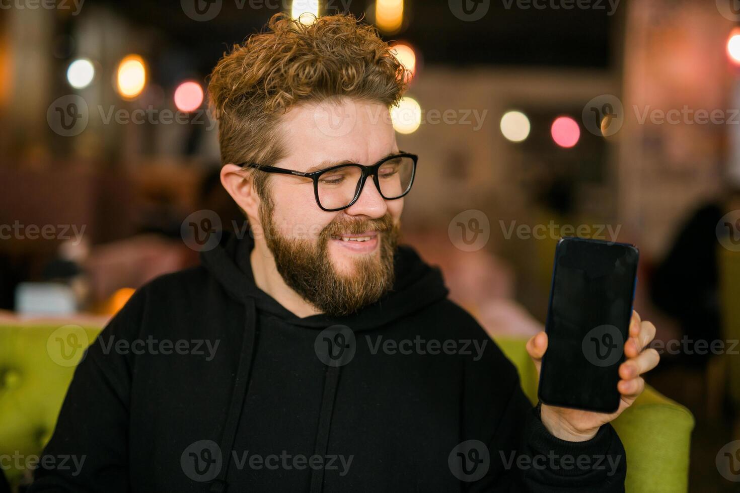 Satisfied man with dark beard holding smartphone and showing his favorite mobile app Male programmer has developed a cool application. photo