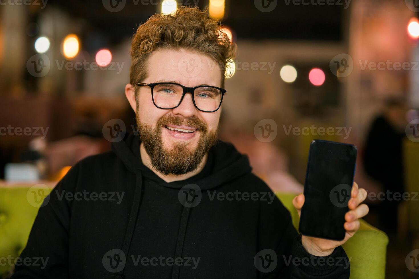 Satisfied man with dark beard holding smartphone and showing his favorite mobile app Male programmer has developed a cool application. photo