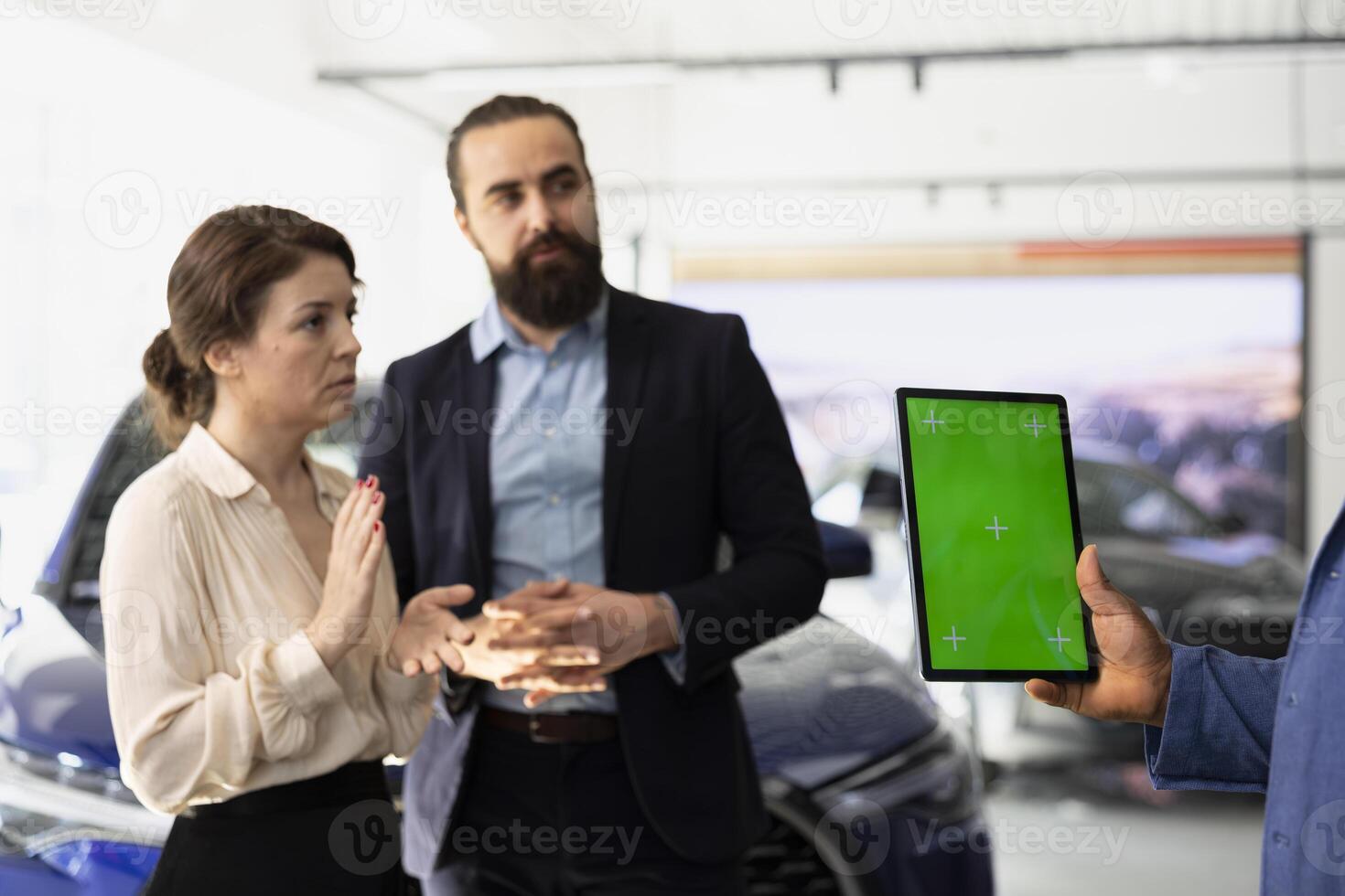 Car sales executive showcasing dealership vehicles to client using green screen tablet. Showroom salesperson helping customer choose automobile using chroma key device, comparing models photo