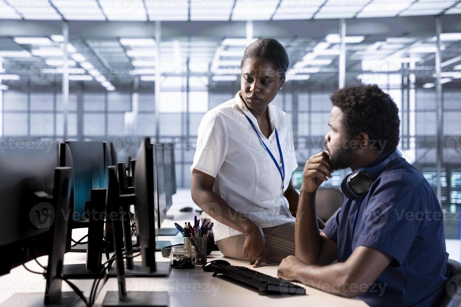 Supervisor checking on data center employee creating technical documentation for software applications. Manager supervising IT expert working in server room maintaining databases photo