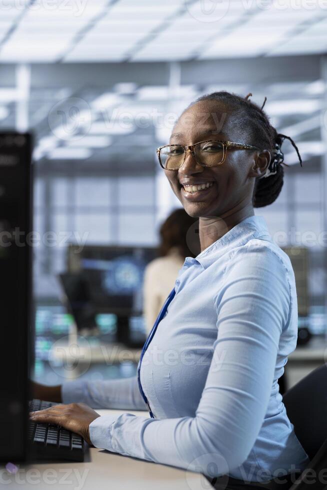 Portrait of smiling technician in data center coordinating deployment of server architecture, improving data processing speed. Happy woman in server hub configuring and testing equipment photo