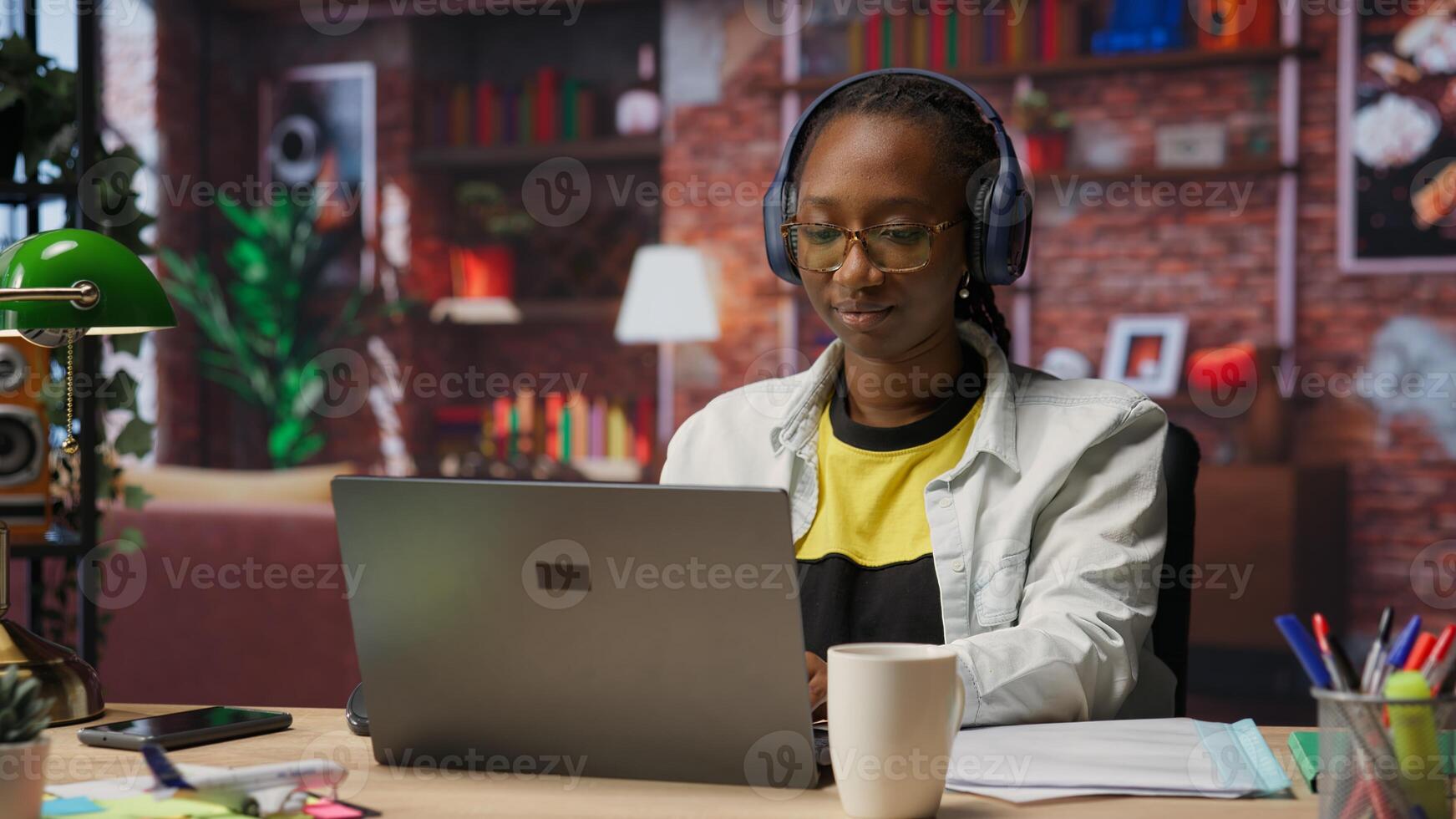Teleworker listening music while typing on notebook keyboard in home office, writing emails. Remote employee wearing headphones using laptop, finishing project tasks, camera B photo