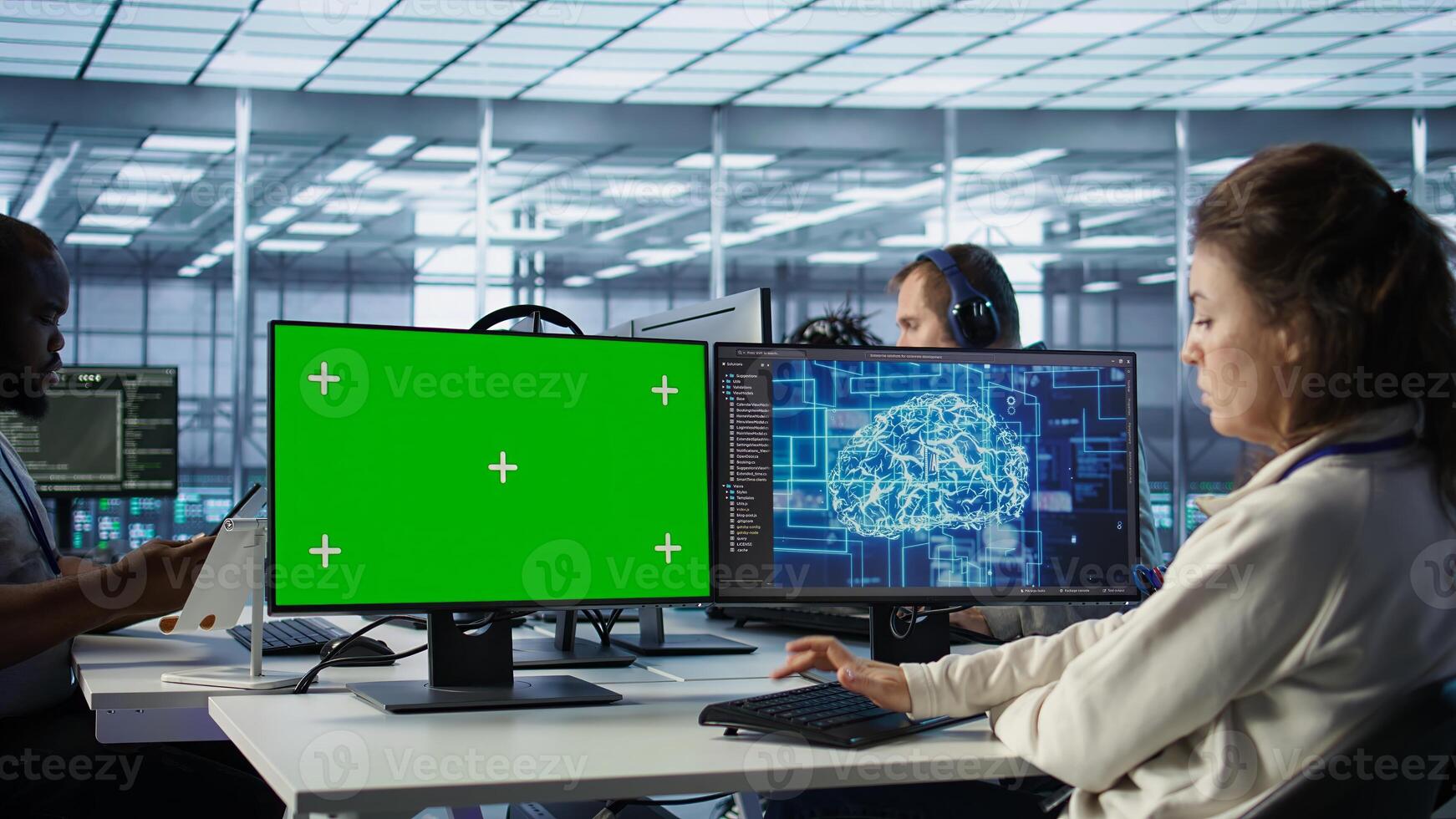 IT support workers in AI data center coding on green screen computers, upgrading equipment. Multiethnic team of engineers at PC desk overseeing server clusters using mockup monitors, camera B photo