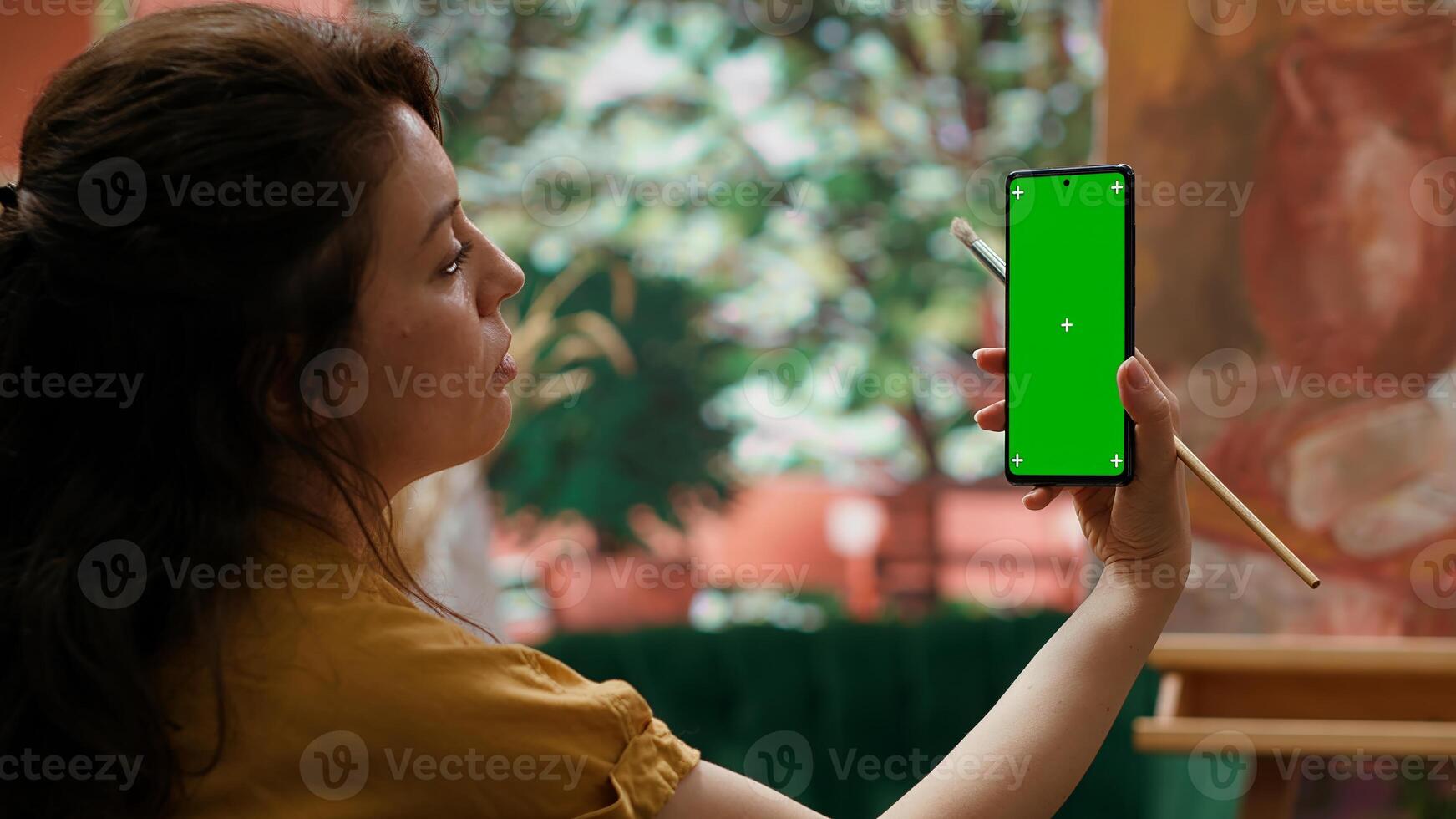 Young woman looking at chroma key display and at her rustic masterpiece, feeling proud and confident with her paintwork for the art gallery. Artist enjoying her hobby for leisure. Camera A. photo