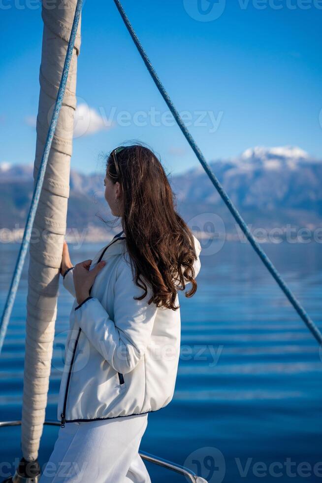 Portrait of young woman on bow of the yacht during sailing in the morning in winter time in Adriatic sea, yacht life and yachting concept. High quality photo