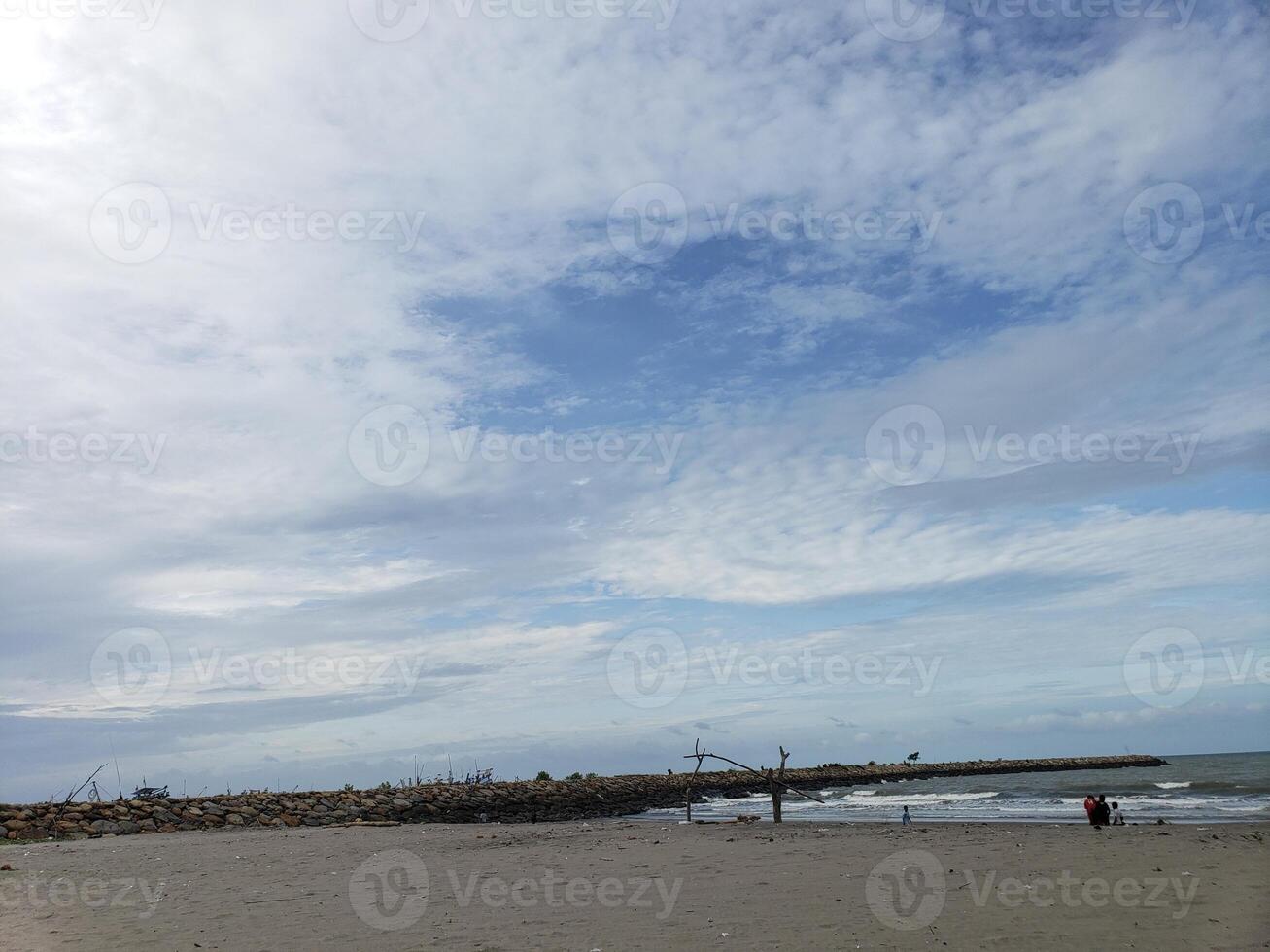 Beach with a rock wall, waves, and people walking photo