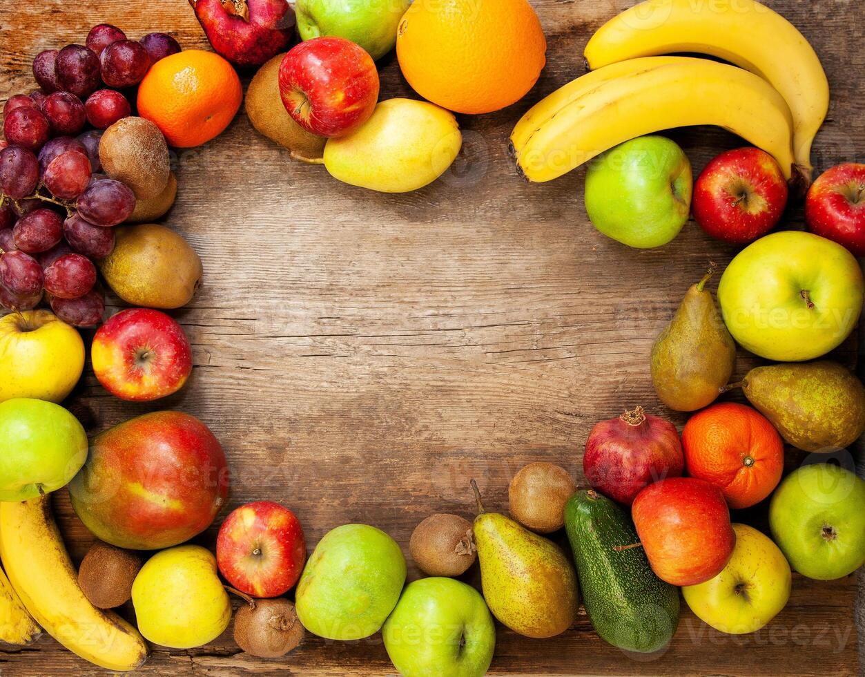 Frame from multi-colored different fruits on a wooden background. Harvest fruits top view. Bananas, apples and pears. Lemon, mango, avocado and grapes. photo