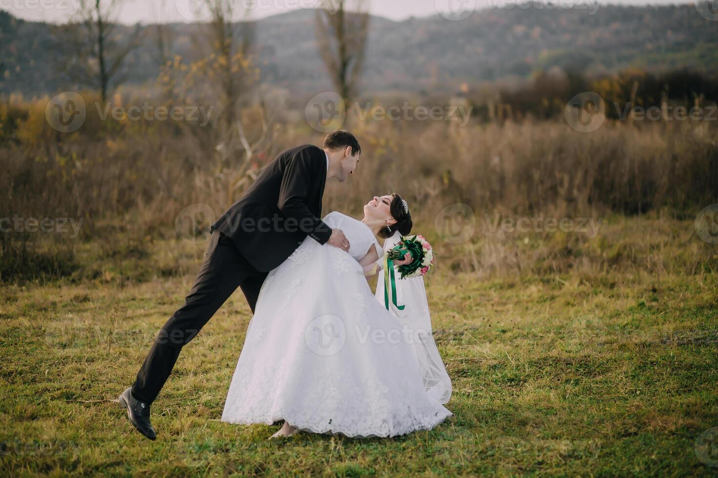 A bride and groom are playing in the grass. photo