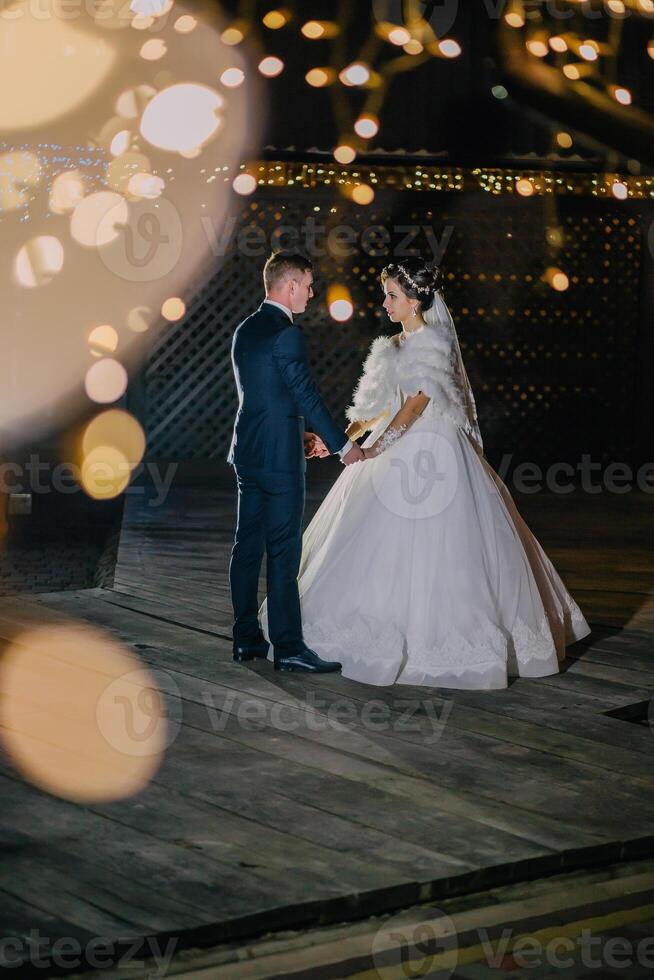 bride and groom stand on the background of garlands. Night wedding ceremony with candles photo