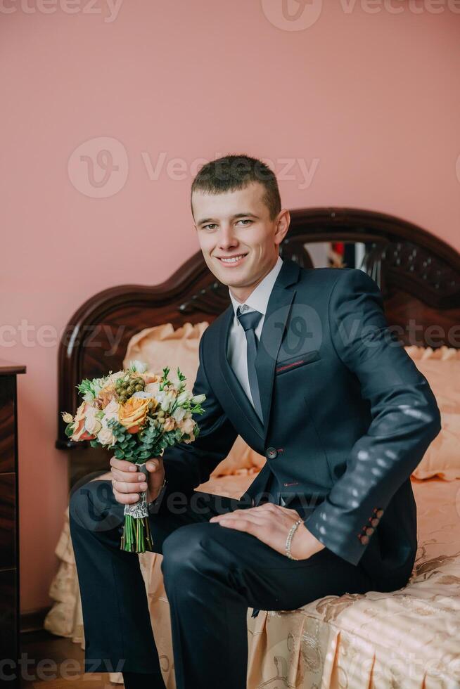 A man in a suit and tie is sitting on a bed with a bouquet of flowers in his lap photo