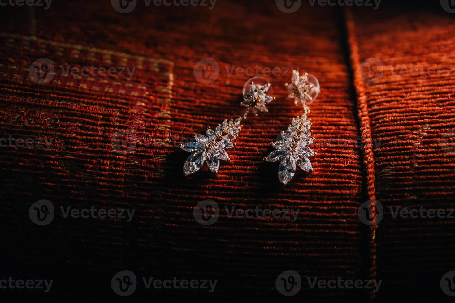 A pair of earrings with a leaf design are sitting on a red cloth photo