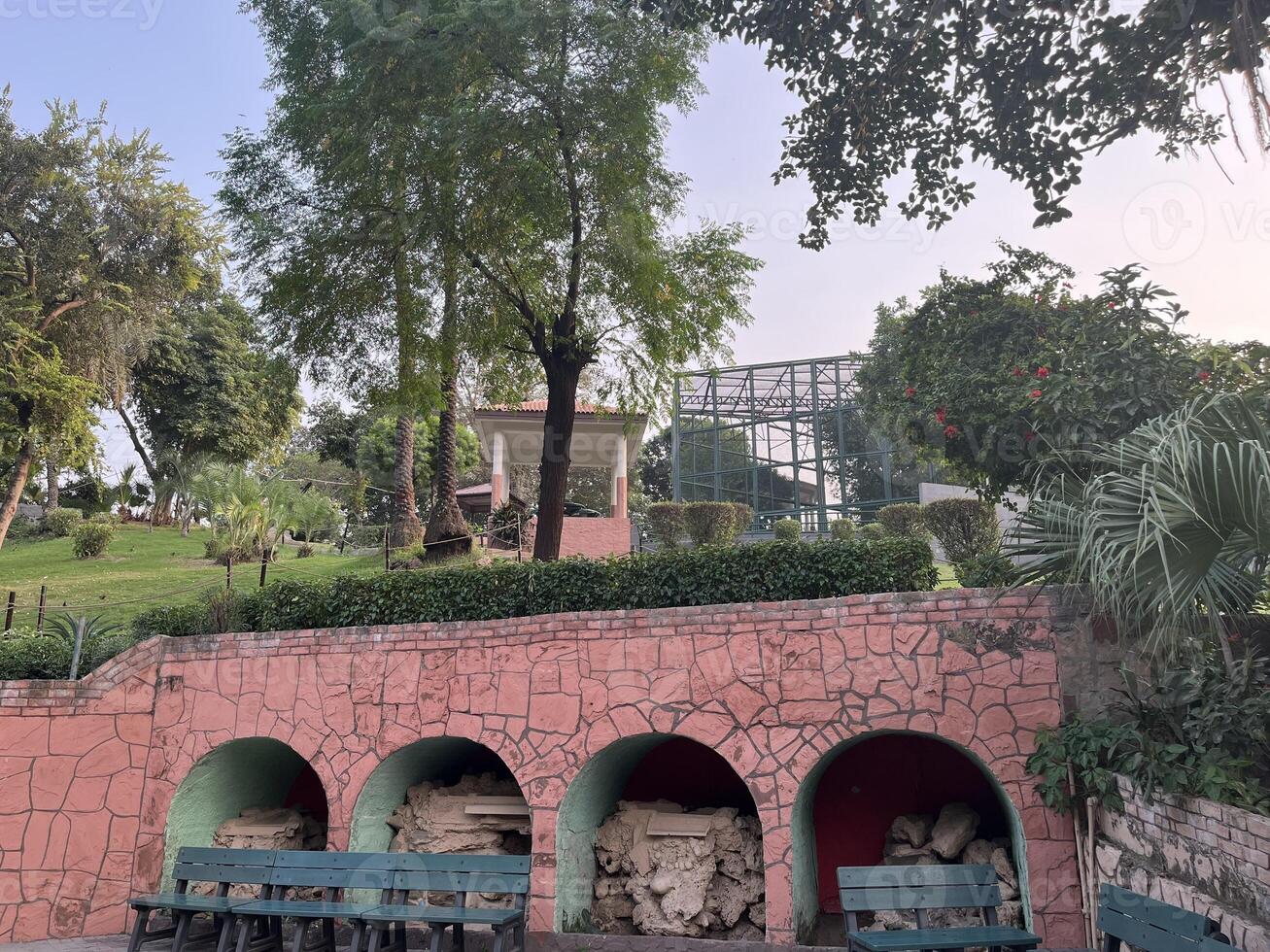 a pink building with several benches and trees in Lahore on 10-10-2024 photo