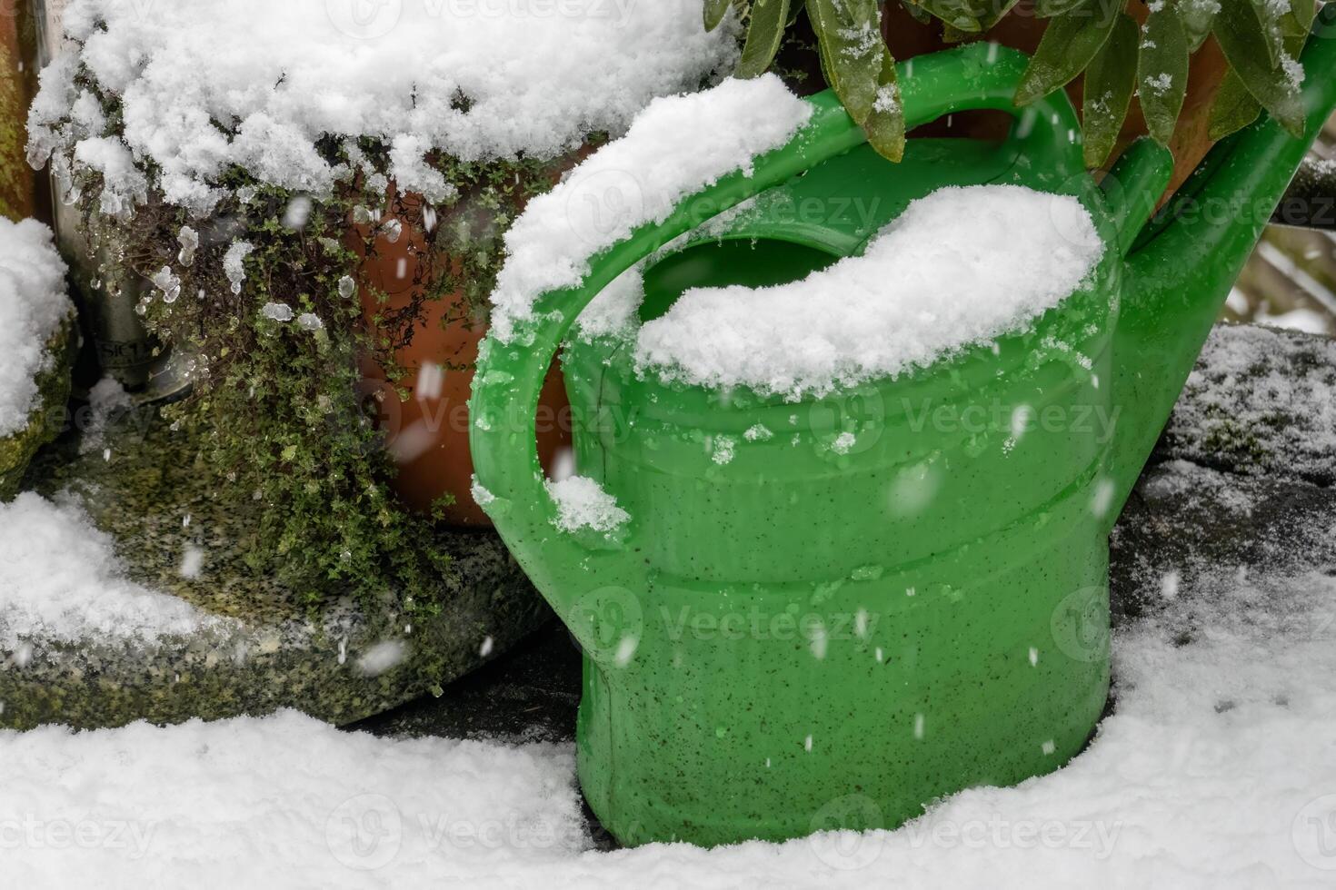 Green watering can covered in snow during winter snowfall photo