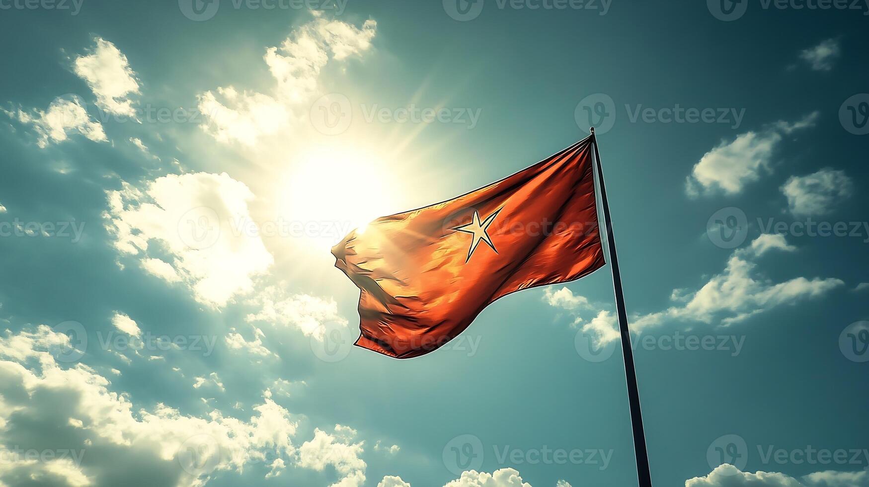 Dramatic View of Red Flag Against a Deep Blue Sky with Sunlight Piercing Through photo