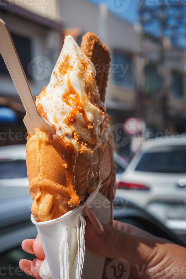 Hand Holding Soft Serve Ice Cream with Caramel and Biscuit Topping photo