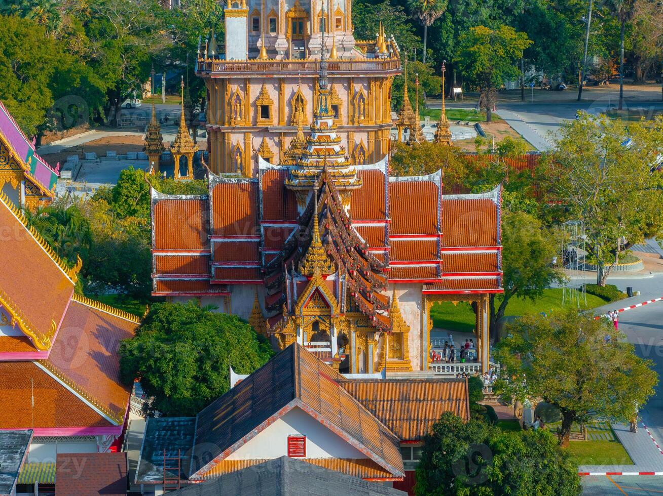 Wat Chalong temple in Phuket, Thailand, features ornate golden details, red tiled roofs, a towering pagoda, and lush greenery in a serene setting. photo