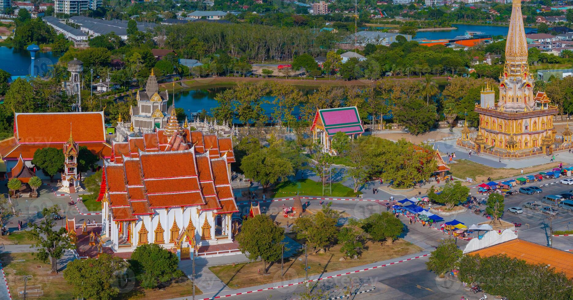 Wat Chalong in Phuket, Thailand, featuring the Grand Pagoda with golden details, red roofed temple, lush greenery, a pond, and surrounding structures. photo