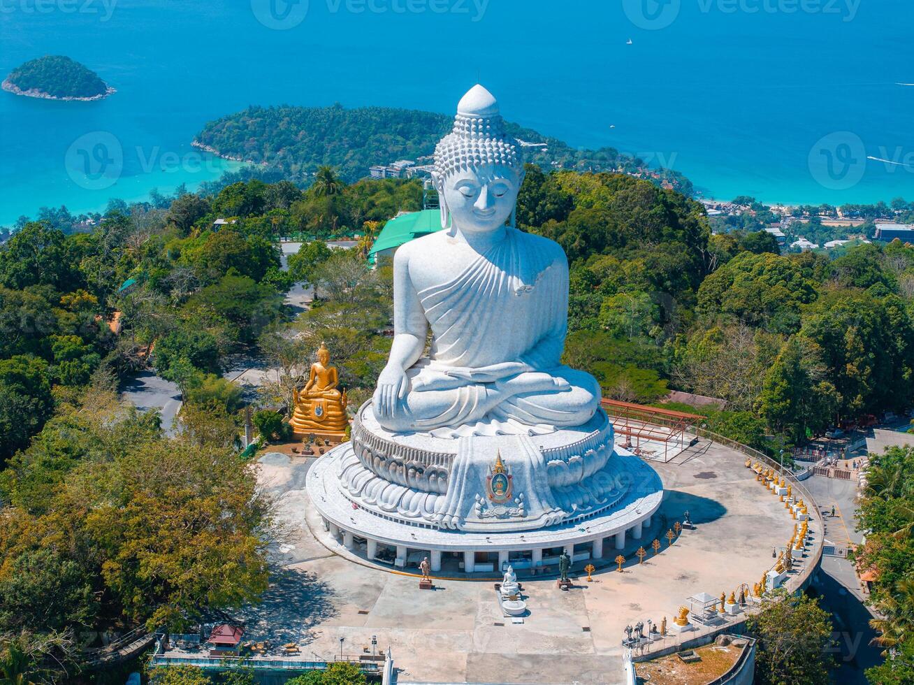 The iconic Big Buddha statue in Phuket, Thailand, surrounded by greenery, with a golden Buddha nearby and turquoise waters visible in the distance. photo