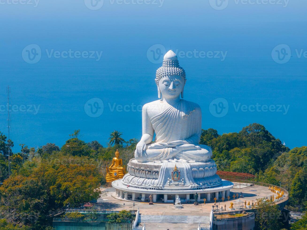 The iconic white marble Big Buddha statue in Phuket, Thailand, stands on a hilltop with ocean views, surrounded by greenery and a paved platform. photo