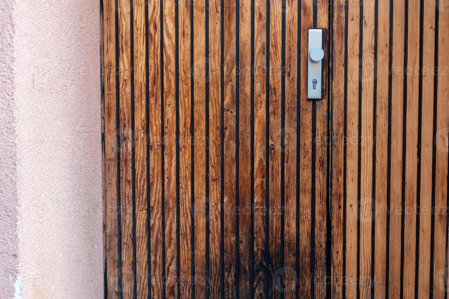 Wooden door with vertical slats and lock in a warm-toned structure during daylight photo