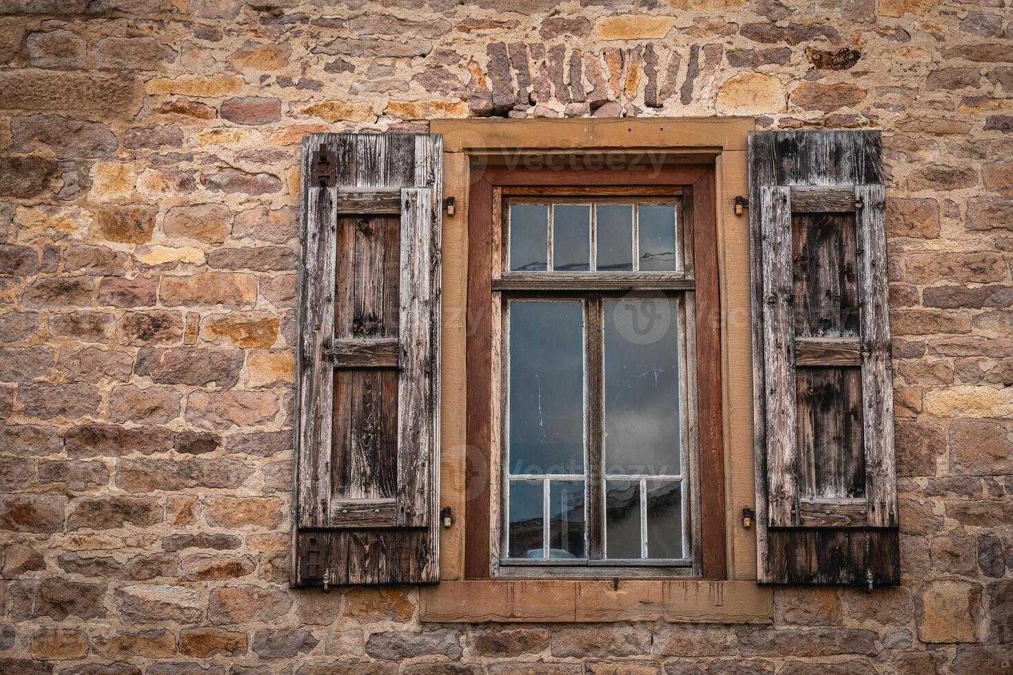 Rustic wooden window framed by aged stone wall reflects calm sky in a quaint rural setting photo