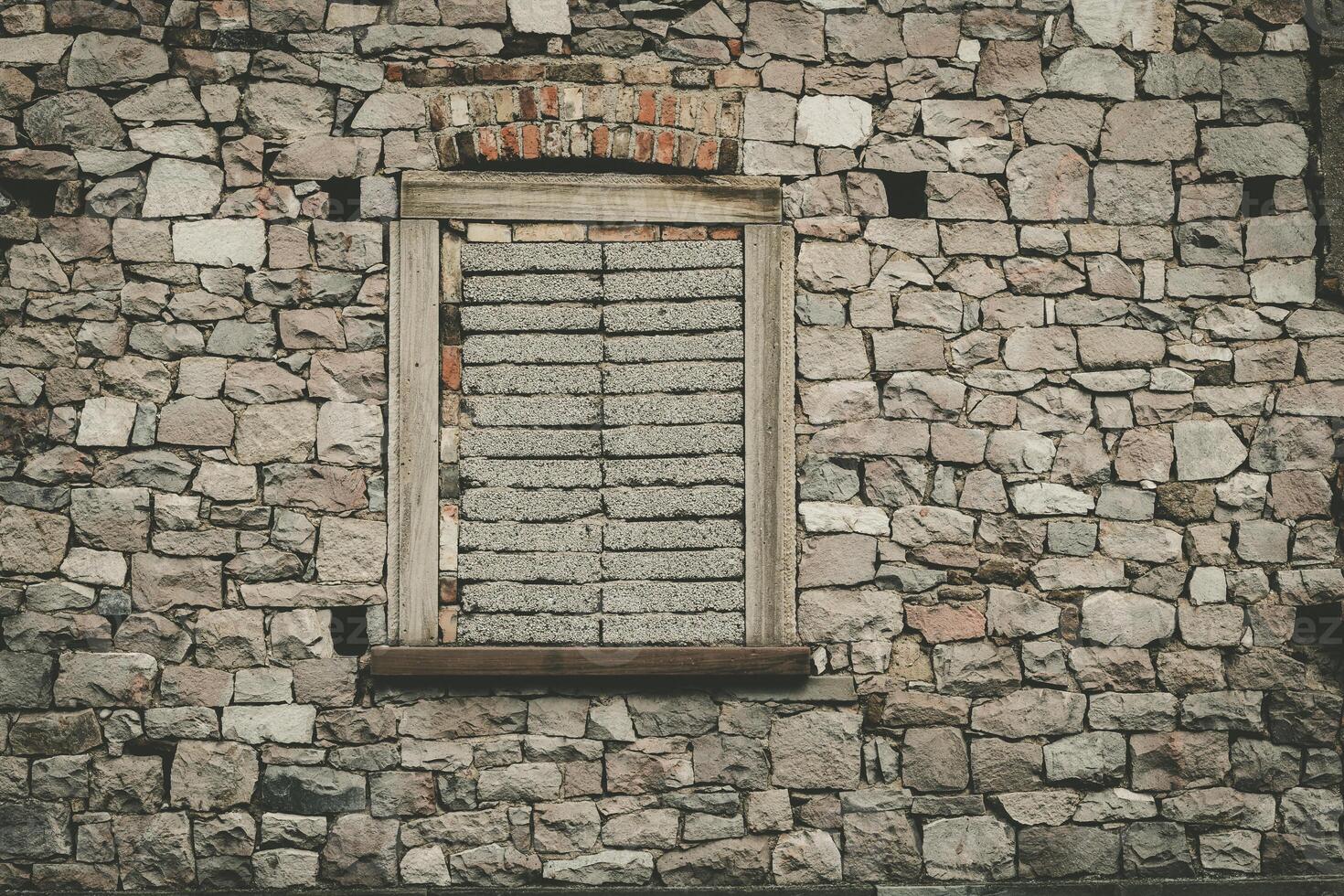 Stone wall with boarded window showcasing aged textures and rustic charm in an abandoned setting photo