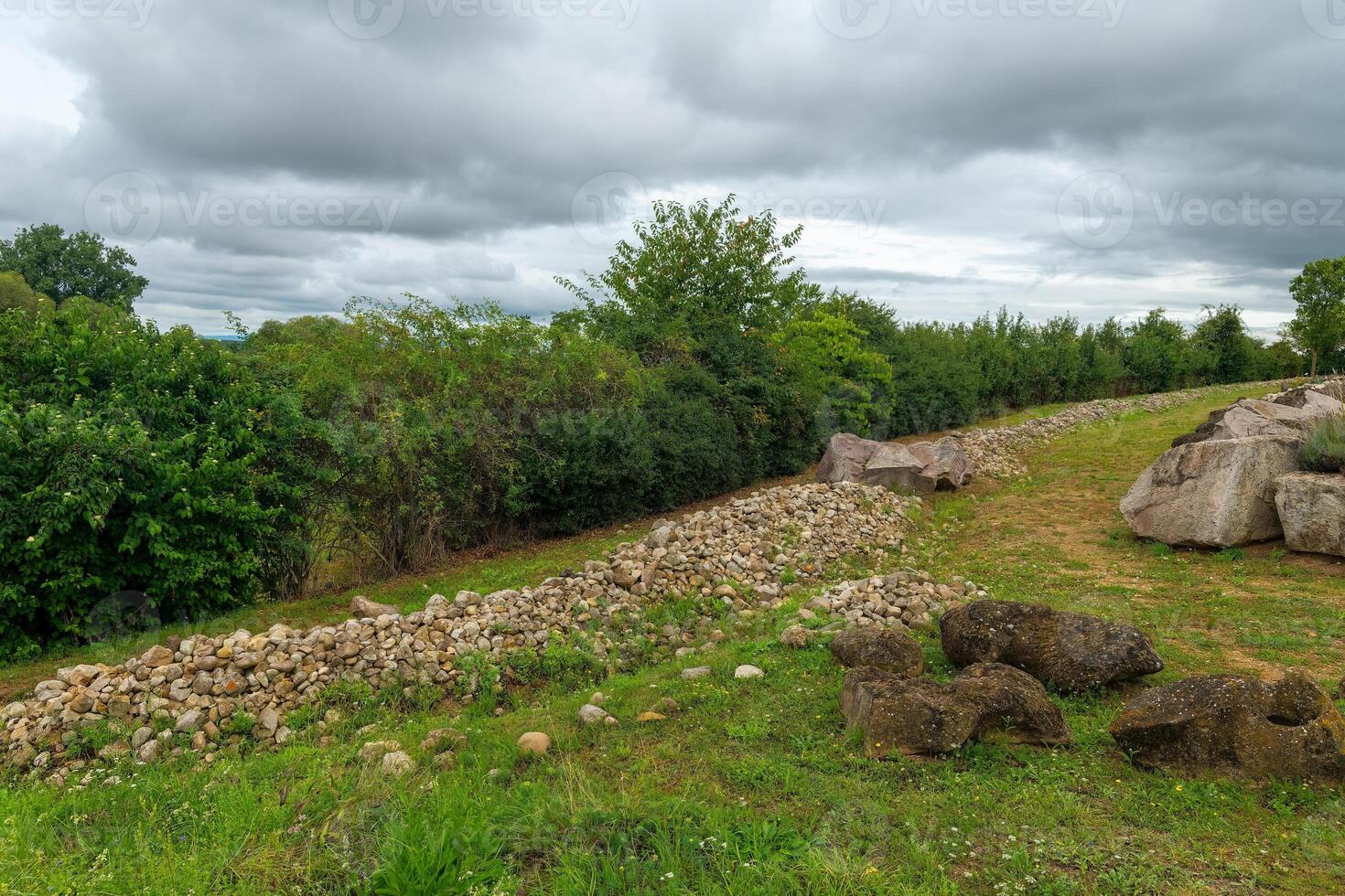 Stone wall borders a green landscape under overcast sky in rural setting during late afternoon photo