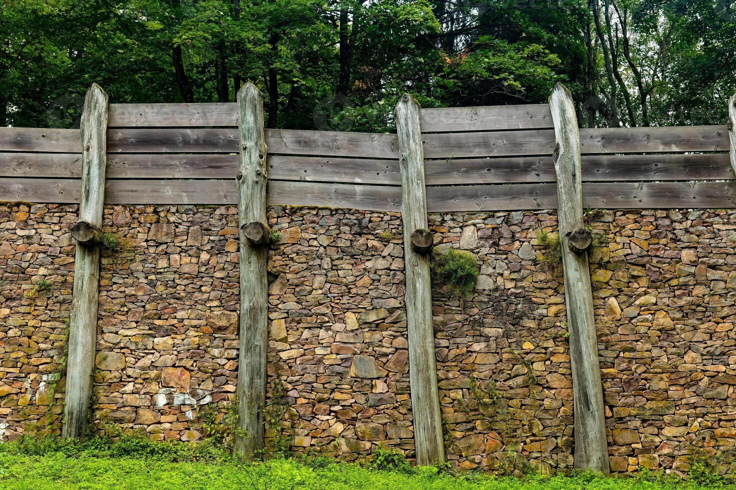 Reconstruction of ancient fortification featuring wooden palisades and stone wall in a forested area photo