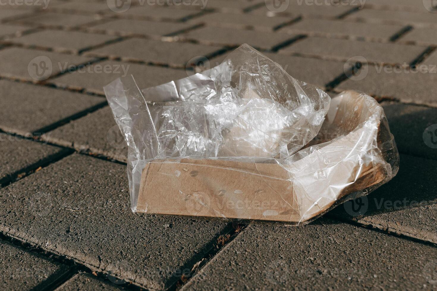 Discarded cardboard box wrapped in plastic on pavement during daylight in an urban area photo