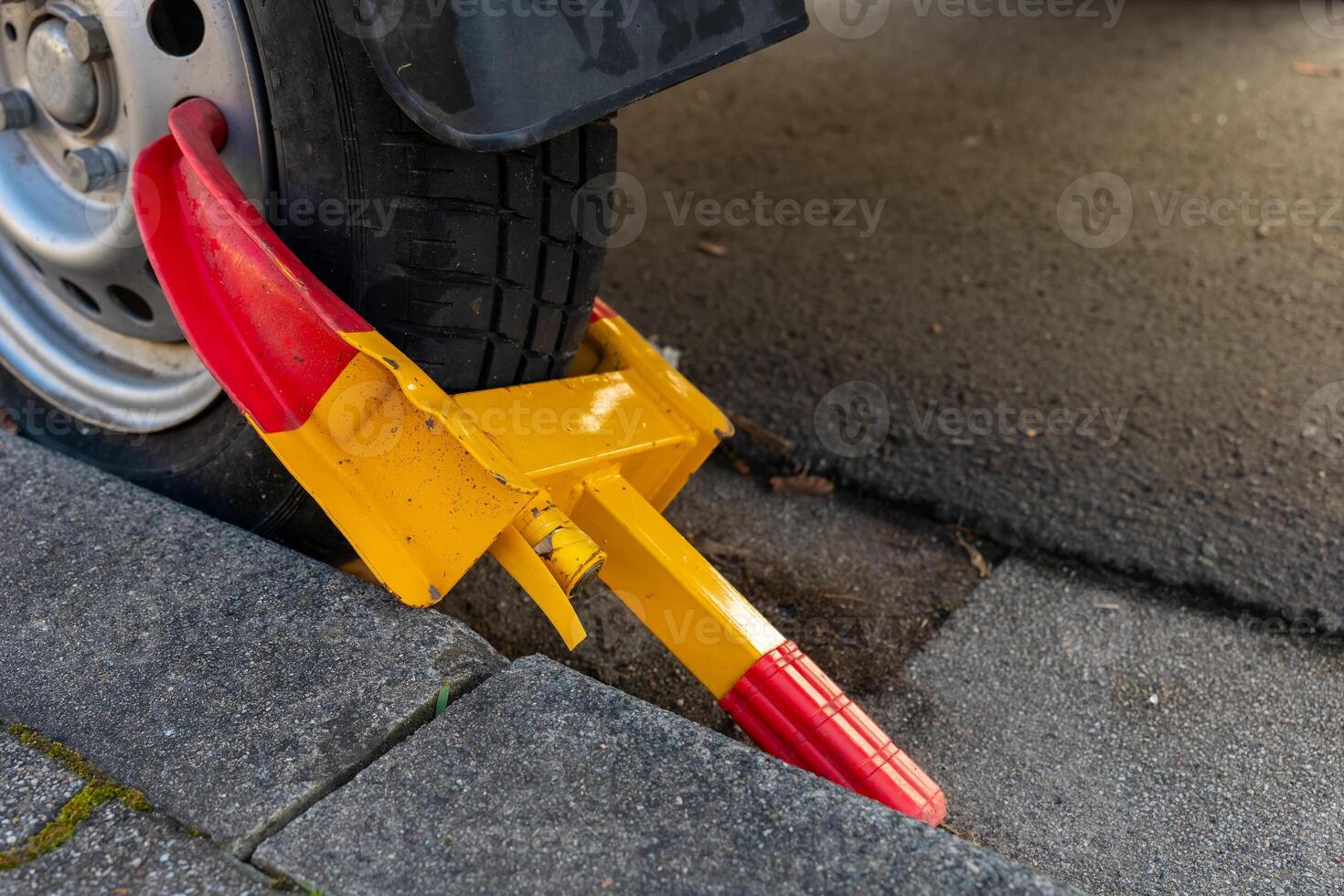 Vehicle immobilized with a bright yellow and red wheel clamp on a city street in the afternoon sun photo